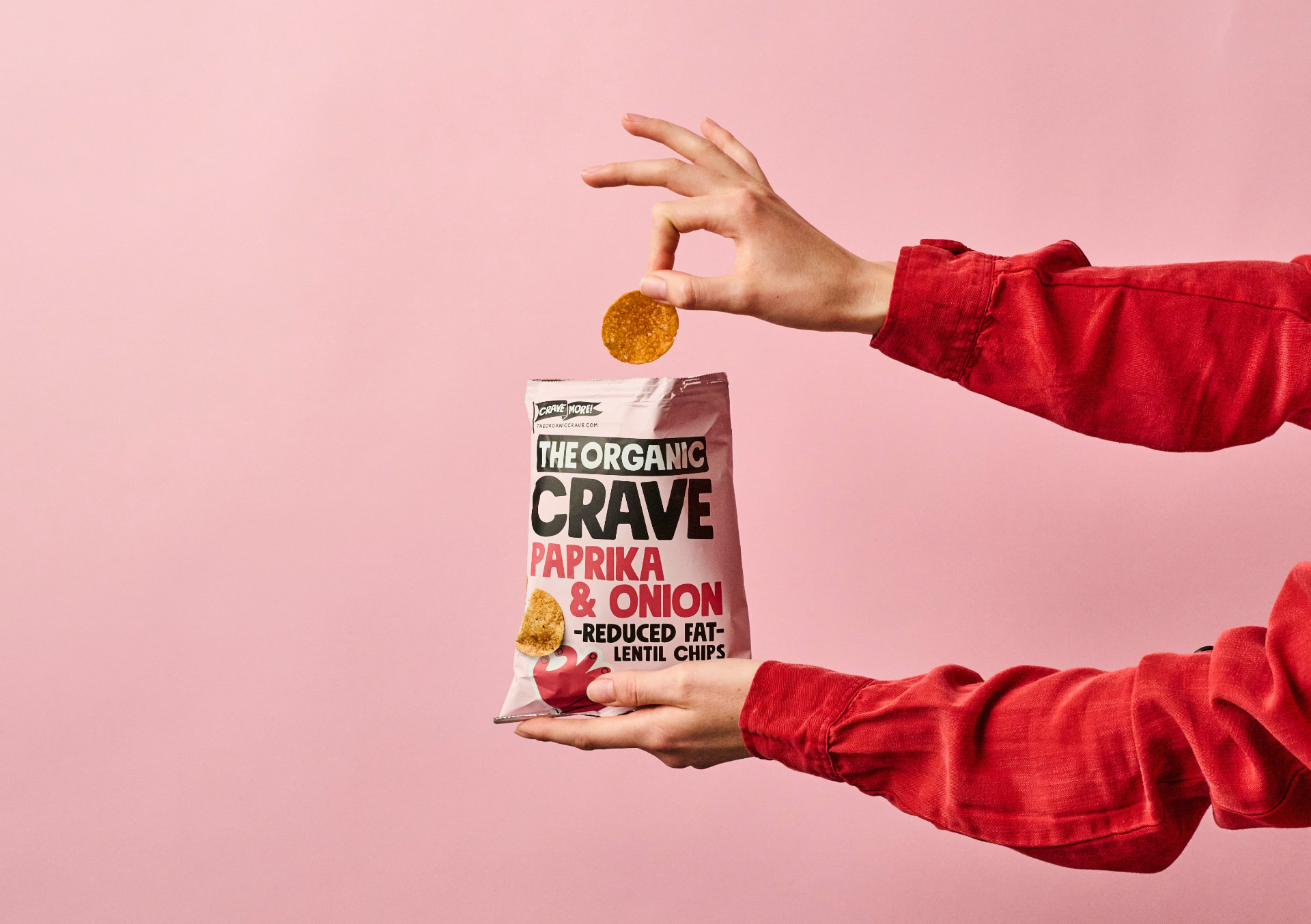 A hand dropping a lentil chip into a bag of organic snacks